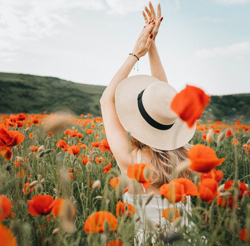 lady in hat standing with raised arms among red poppy flowers